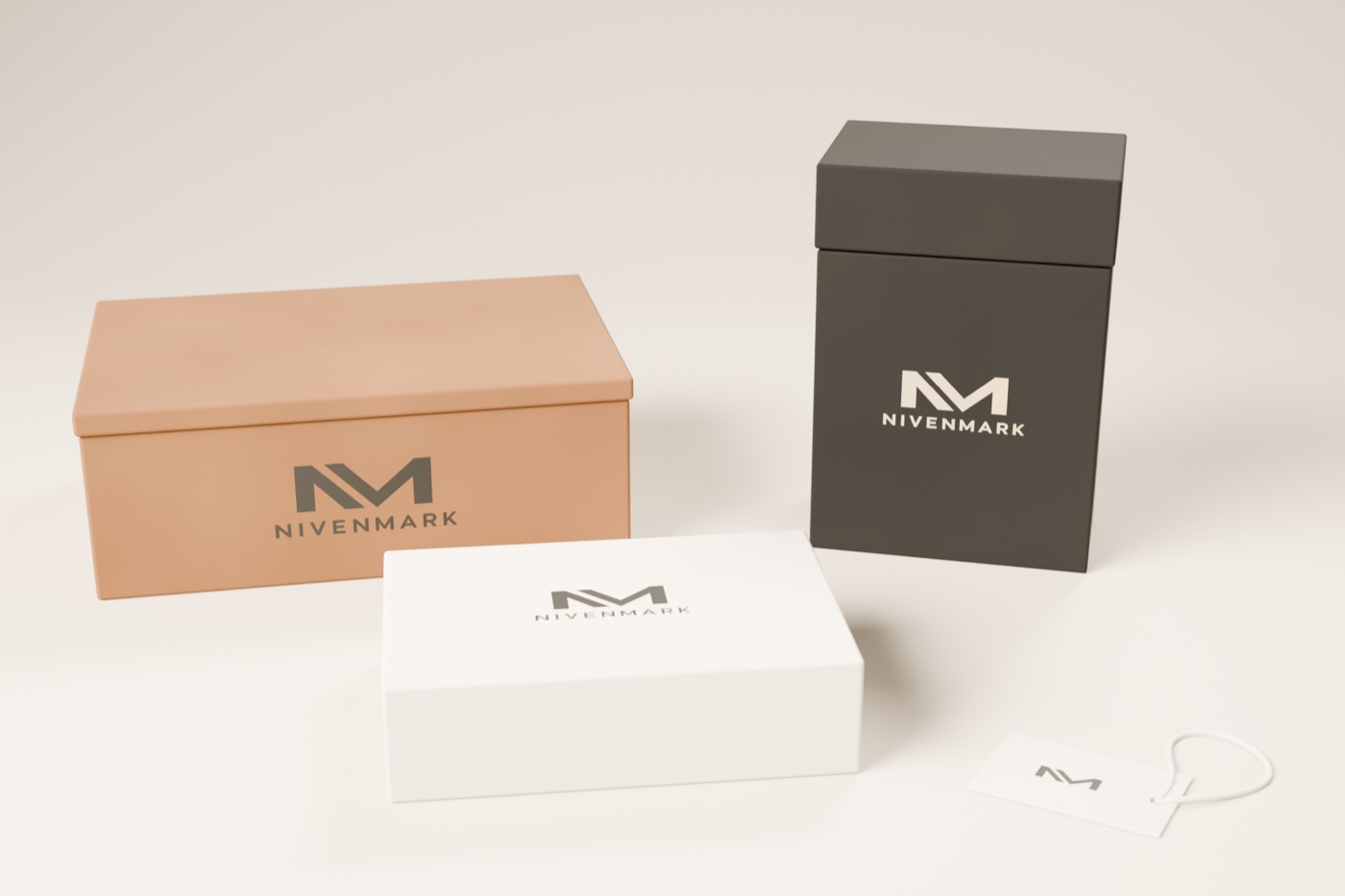 Sistema de empaque de Nivenmark: caja de envío kraft, cartón rígido carbón con tapa y el logotipo en crema, estuche crema y etiqueta colgante con el monograma y cordón, sobre una superficie clara.